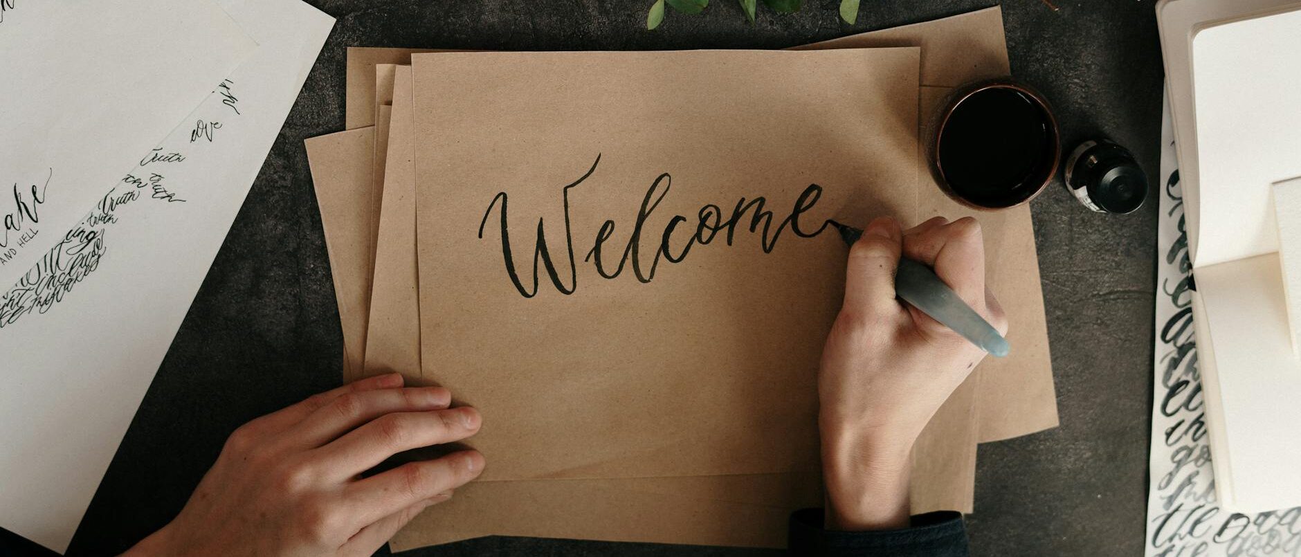 Handwriting a welcome card with calligraphy on craft paper, surrounded by art supplies.